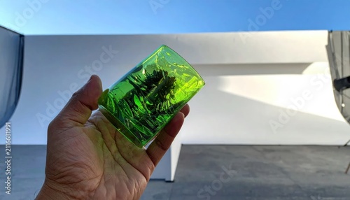 A hand holding a vibrant green translucent glass block against a white studio backdrop.