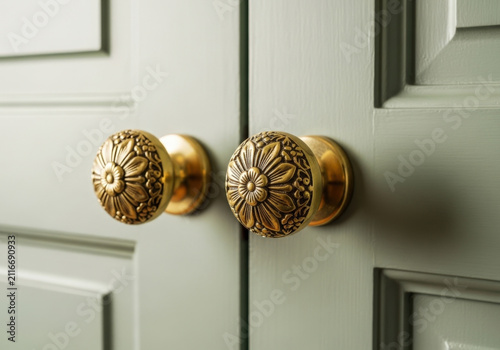 Close up of vintage style brass door handles with ornate floral engraving mounted on light green painted wooden cabinet doors in elegant home design.