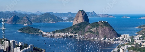 Fotografie The sweeping view of Sugarloaf Mountain highlights its imposing shape rising above Guanabara Bay, featuring green slopes, blue waters, and the sprawling city