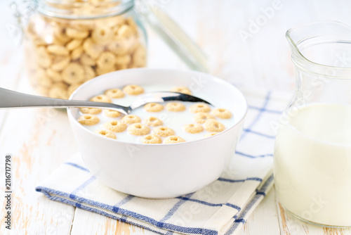 Making a healthy breakfast cereal using corn rings and milk on a white table.