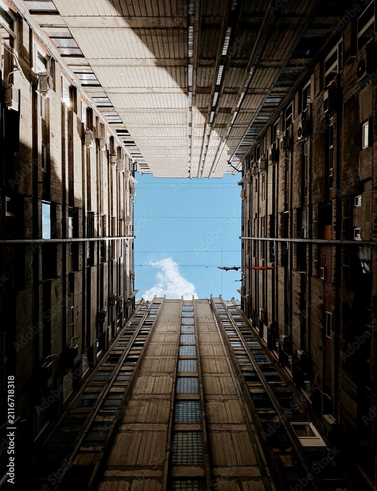 Obraz premium Low angle view looking up at brutalist concrete apartment buildings framing a square piece of blue sky.