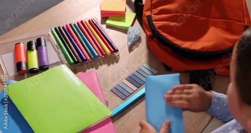 Little girl packing backpack for school at table indoors, closeup