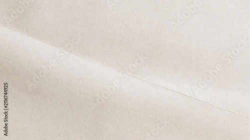 High resolution top-down view of light beige craft paper featuring a soft horizontal fold. The organic material displays subtle fiber flecks and minimalist shadows, perfect for modern aesthetic design