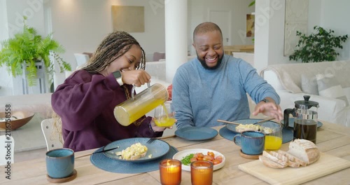 African couple at breakfast, woman picking glass, pouring juice from pitcher into glasses, toasting