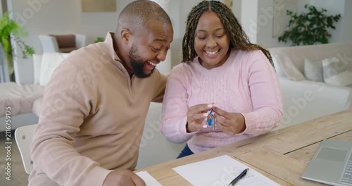 Couple signing contract at home, picking up blue key fob, pointing and celebrating new home