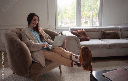 Relaxed young woman using laptop with feet up at home