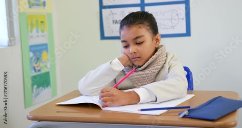 African American child sitting at desk, open notebook, pink pencil leading to writing and thinking