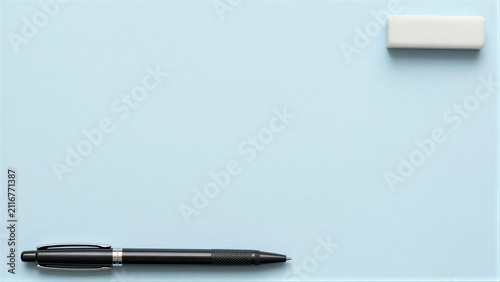 Black pen and white eraser on light blue background, minimalist composition.
