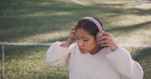 Female child picking up pink headphones on sports turf, putting on and tapping tablet to play