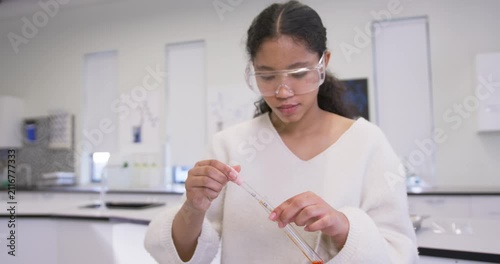 School child with safety goggles pipetting per teacher, checking orange test tube volume at lab