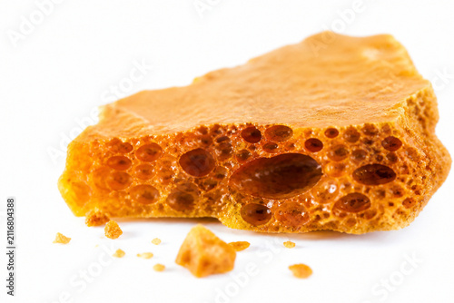 Macro close-up of a broken shard of amber honeycomb toffee showing its porous interior bubbles, resting on pure white. Generative AI photorealistic Halloween studio image isolated on white.