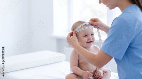 Pediatric healthcare nurse measuring infant head in clinical office with happy baby