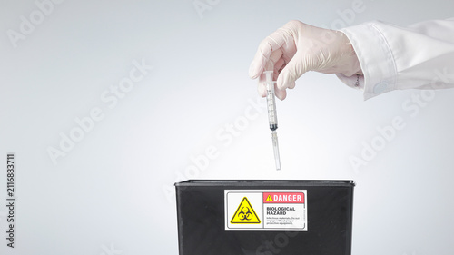 Foto Cautious hand wearing glove drops medical syringe into biohazard container showi