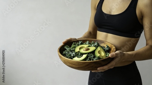 Fit woman presenting kale and avocado salad in wooden bowl