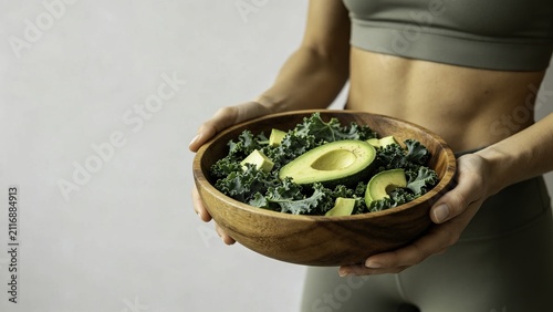 Fit woman presenting kale and avocado salad in wooden bowl