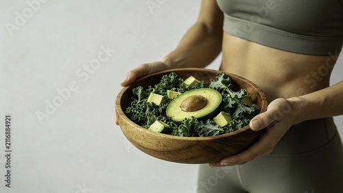 Fit woman presenting kale and avocado salad in wooden bowl