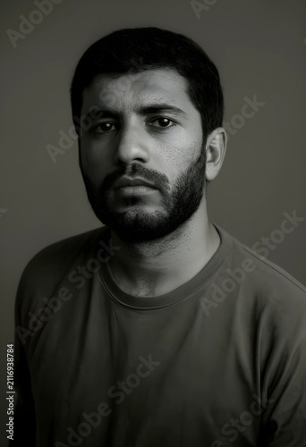 Serious young adult man with a beard and short hair looking directly at the camera in a black and white portrait, the mans face shows a thoughtful expression, his eyes and facial hair