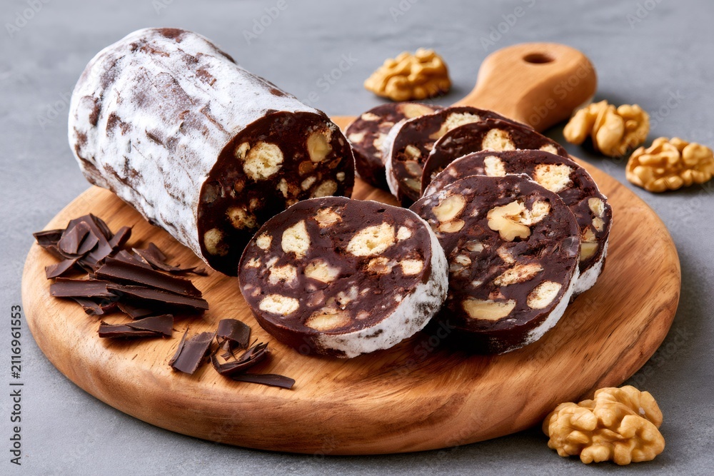 Fototapeta premium Chocolate salami with walnuts and powdered sugar sliced on wooden board
