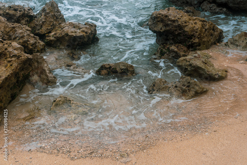 Rocky Beach Shoreline With Waves Washing Over Sand And Weathered Coastal Rocks At Low Tide