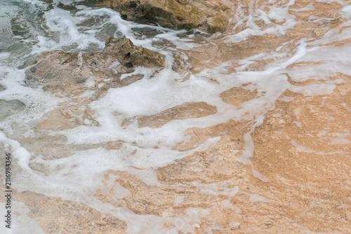 Foamy Ocean Waves Washing Over Rocky Sandy Shoreline With Sea foam Patterns And Textured Sand