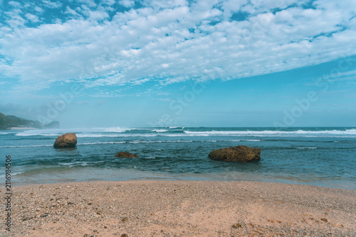 Calm Rocky Beach Seascape With Blue Ocean Waves And Pebbled Shore Under Cloudy Sky