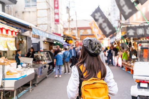 Young female tourist walking along busy food stalls, enjoying street food tour at Tsukiji Outer Market in Tokyo, Japan