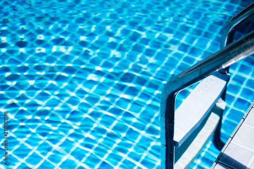 Photography Metal pool ladder descending into vibrant, rippling blue water of a sunlit pool