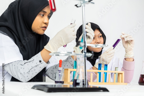 Two Muslim female scientists wearing hijab working in a chemistry laboratory with glassware and chemical solutions. Perfect for STEM education, research, science, healthcare, and biotechnology concept