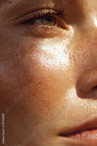 Summer time. Close-up of a young woman's face highlighting freckles and glowing skin texture under natural light. summer vibes light concept