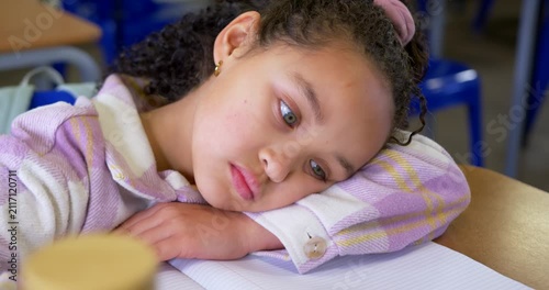African American child lowering gaze resting head at school desk with notebook in pink top dozing