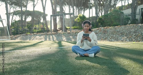 Female child sitting cross-legged on turf tapping tablet, starting audio and wearing pink headset