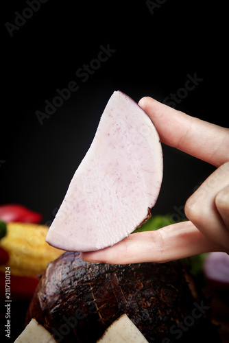 Quadro su tela Hand Holding Fresh Sliced Taro Root Close Up on Black Background