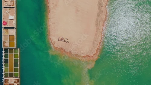 Top-down aerial view of a bulldozer moving sand and earth into the vibrant turquoise water, creating a new artificial land peninsula next to salt evaporation ponds