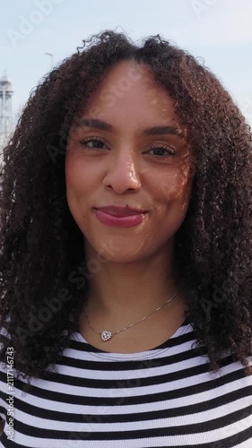 Vertical HD video of smiling Brazilian woman looking at camera on a sunny summer day. Happy young Latin American woman enjoying the outdoors with a confident and natural expression