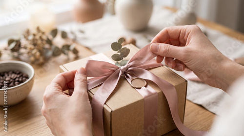 Delicately securing a ribbon on an elegantly wrapped present featuring natural accents in a warm and inviting atmosphere