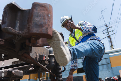 Фотография Train engineer with radio inspecting railcar coupler in yard, Railway technician