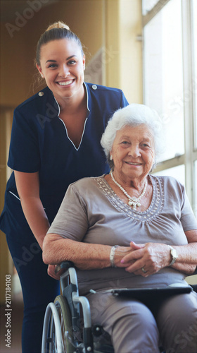 Smiling caregiver assisting elderly woman in wheelchair with warm indoor light