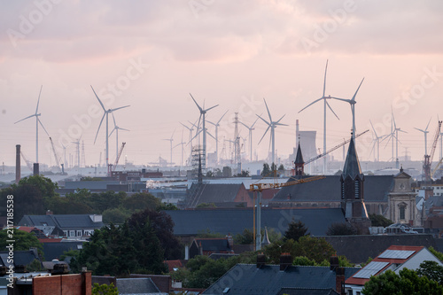 Cuadro en lienzo Rows of wind turbines rise beyond the rooftops and church spires of Ghent under a soft overcast morning sky in Belgium clean energy near the city