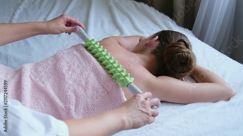 A massage therapist massages a young woman's back with a hand massager