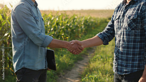 Two farmers shaking hands in green corn field after successful agreement