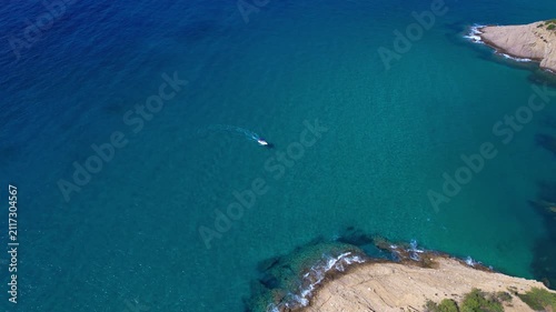 Aerial drone view of a powerful speed boat gliding across crystal-clear turquoise water, creating a striking white wake. Perfect representation of luxury travel, freedom, summer adventure.