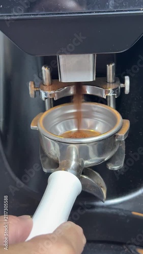 Coffee preparation, espresso grounds falling into a metal portafilter basket. Close-up macro shot showing professional barista workflow at a cafe station.