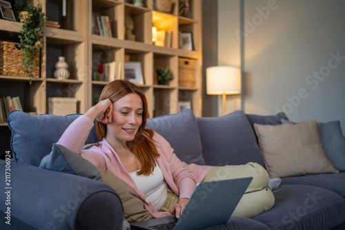 Fotografie Young woman relaxing on sofa using laptop at home