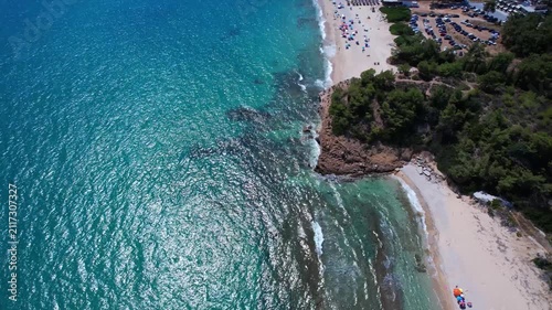 Beautiful aerial view of a sandy beach with crystal clear sea, turquoise water and visitors enjoying swimming and paddleboarding on Thassos Island, Greece.