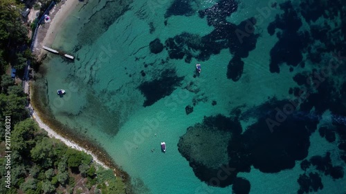 Aerial drone of a peaceful beach in Thassos, Greece, featuring transparent turquoise water, paddleboards, swimmers and a beautiful Mediterranean coastline.