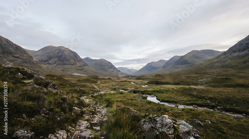 Rugged highland valley terrain featuring winding streams and towering peaks under a cloudy overcast sky providing a wide panoramic view of the vast wilderness landscape during the autumn season