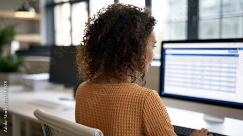 Using customer relationship management software to update client records and follow-up tasks unfolds at an organized workstation where a faceless young African American professional woman