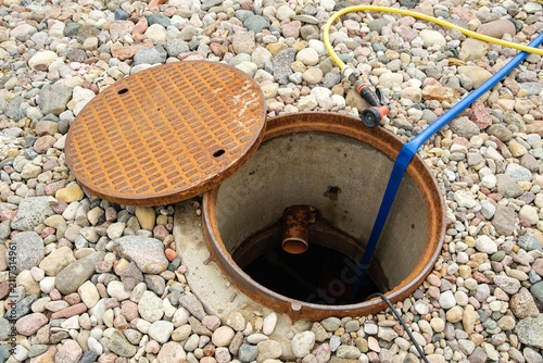 An open sewer manhole. A service cleaning of blocked sewer. A concrete septic tank with a plastic pipe. Rinse and pumping water out. Maintenance work, utility service, underground infrastructure.