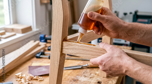 Hand squeezing liquid wood glue from squeeze bottle into mortise and tenon joint of wooden chair frame component
