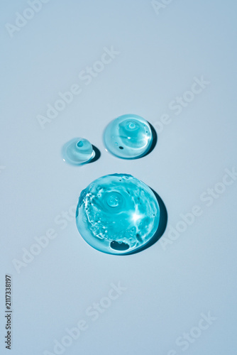 Fotografie Blue Cosmetic Gel Drops with Air Bubbles over Light Pastel Blue Commercial Backg